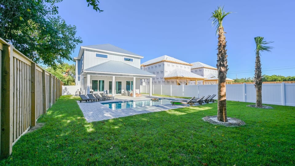 Wide shot of the pool, lawn, and surrounding fence under a clear sky.