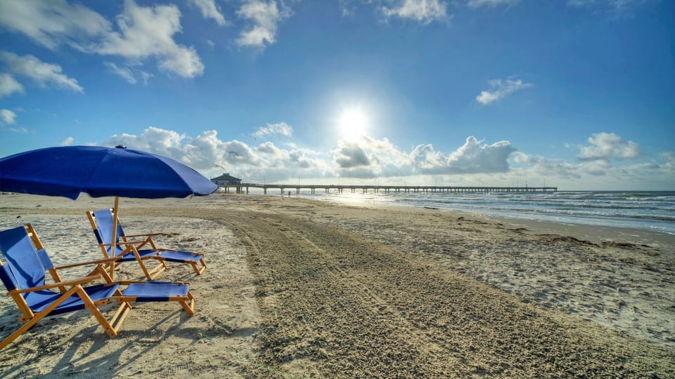 Wide view of the beach with lounge chairs and the pier in the distance.