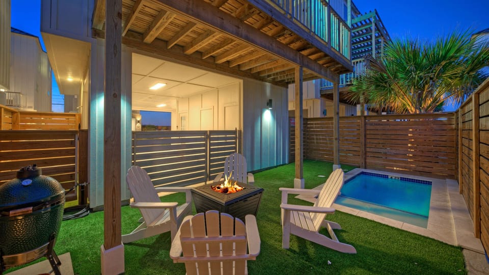 Evening view of the private backyard with a firepit, plunge pool, and turf lawn.
