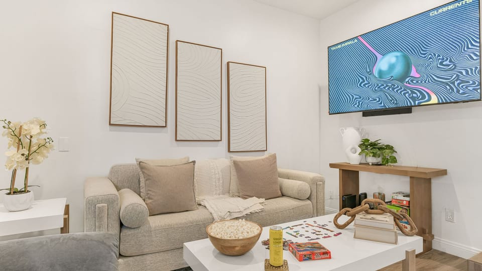 Modern living room with a neutral-toned sofa, large wall-mounted TV, and minimalist artwork.