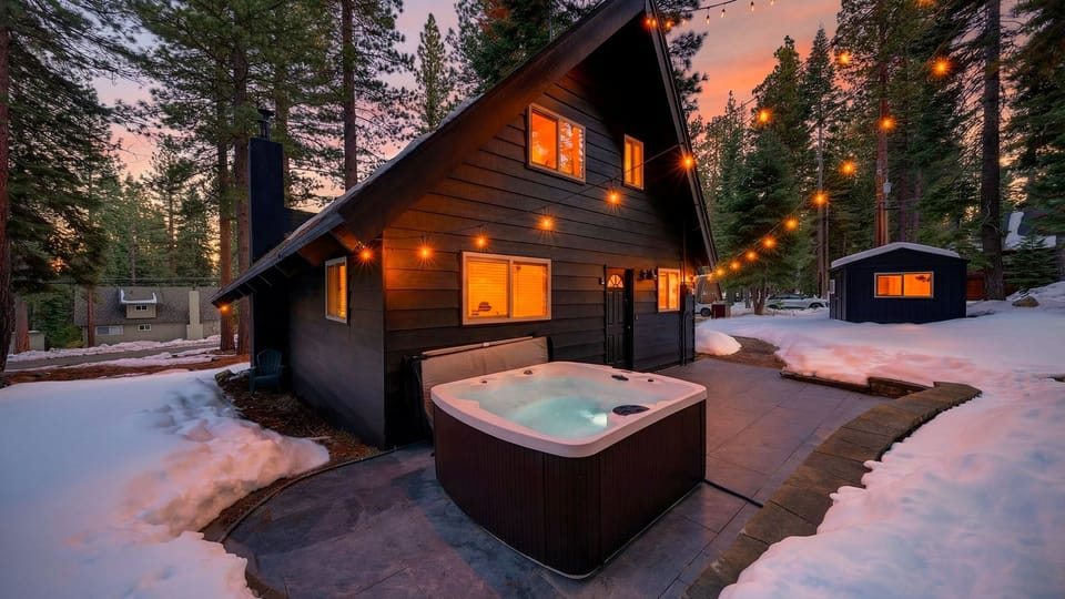Charming A-frame cabin glowing at twilight with an outdoor hot tub.