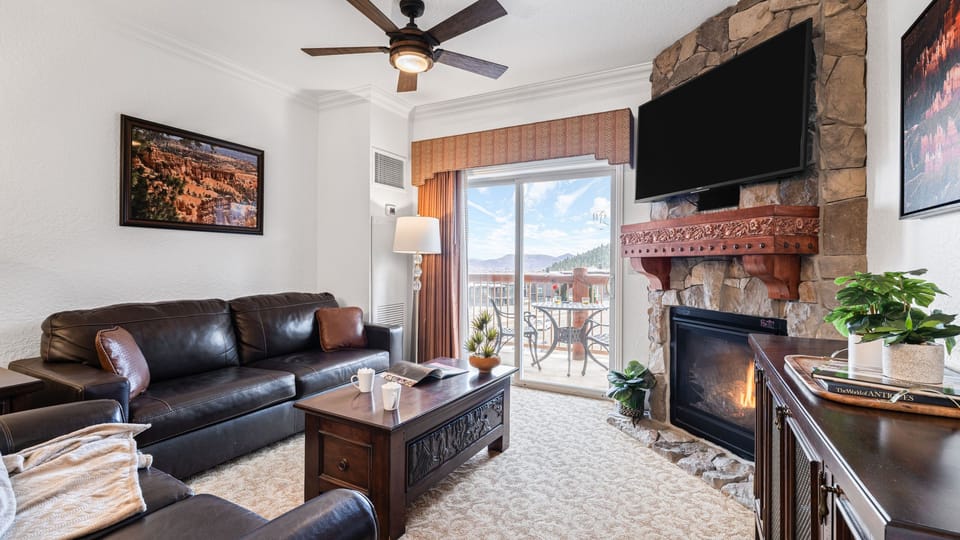 Cozy living room featuring leather seating, a stone fireplace, and balcony access.