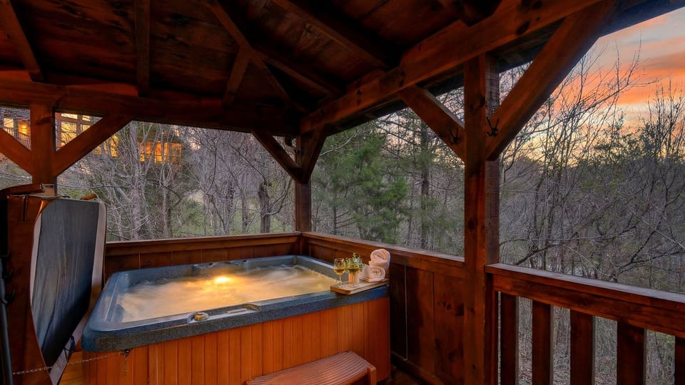 Covered deck featuring a private hot tub with a forest view.