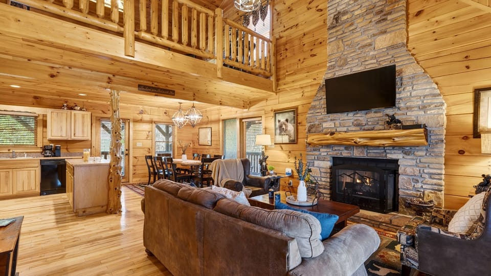 Open-concept living area with a stone fireplace, leather seating, and loft views.