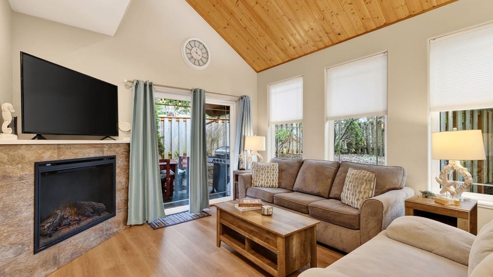 Bright living room with vaulted wood ceilings, fireplace, and patio access.