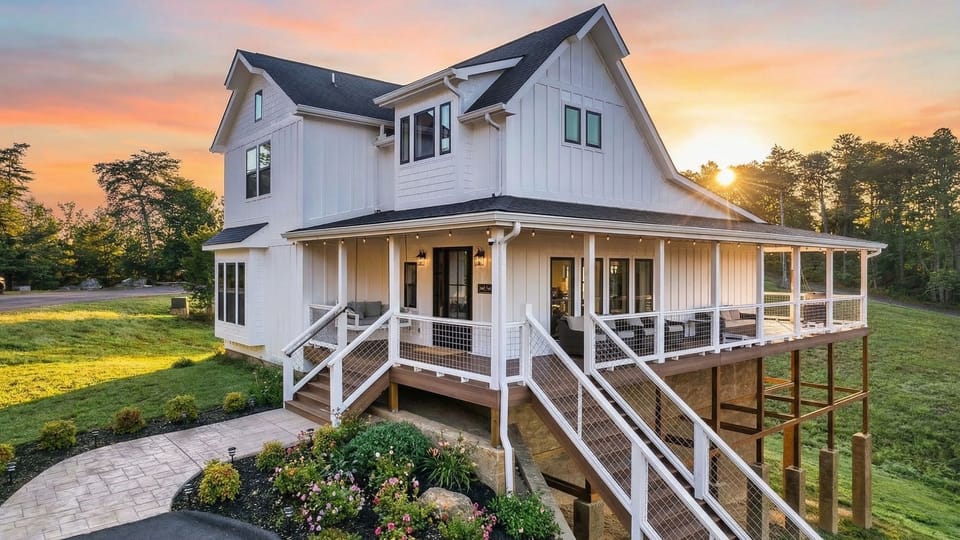 Golden hour at its best—this mountain home glows at dusk, with a wraparound porch, warm interior light, and peaceful Smoky Mountain.