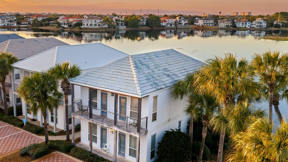 Aerial view of this waterfront community, showcasing palm-lined buildings, serene lake views, and easy access to the beach and resort-style amenities nearby.