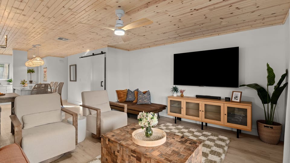 Spacious living room featuring a wood-plank ceiling, wall-mounted TV, and modern coastal decor.