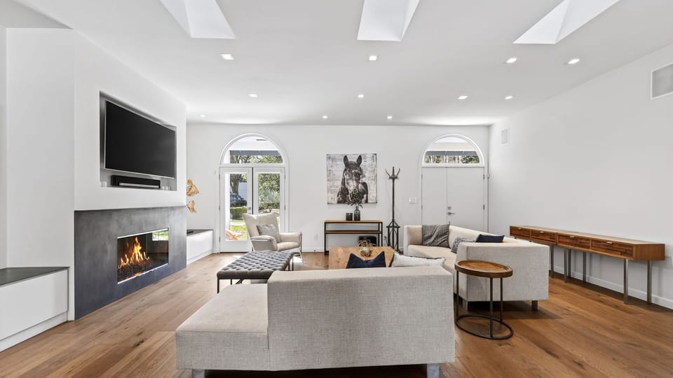 Expansive open-concept living area with skylights, statement fireplace, and seamless indoor-outdoor flow for elevated entertaining.