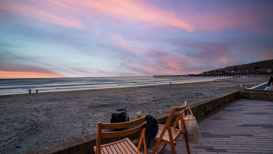Outdoor patio featuring a serene view of the beach at sunset with wooden chairs on the deck.