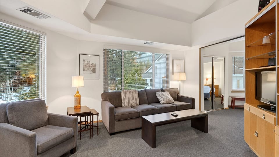 Bright, vaulted living space with large windows, sleeper sofa, and an open flow to the bedroom — perfect for relaxing after a day in Lake Tahoe. (The Ridgeline)