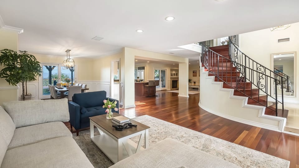 Open-concept living space with sweeping staircase, gleaming hardwoods, and seamless flow into the dining area and kitchen.