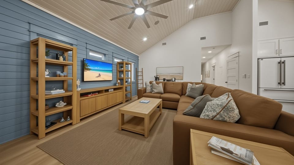 Bright, beachy living room goals—vaulted ceilings, oversized sectional, and a big-screen setup for movie nights after the sand.