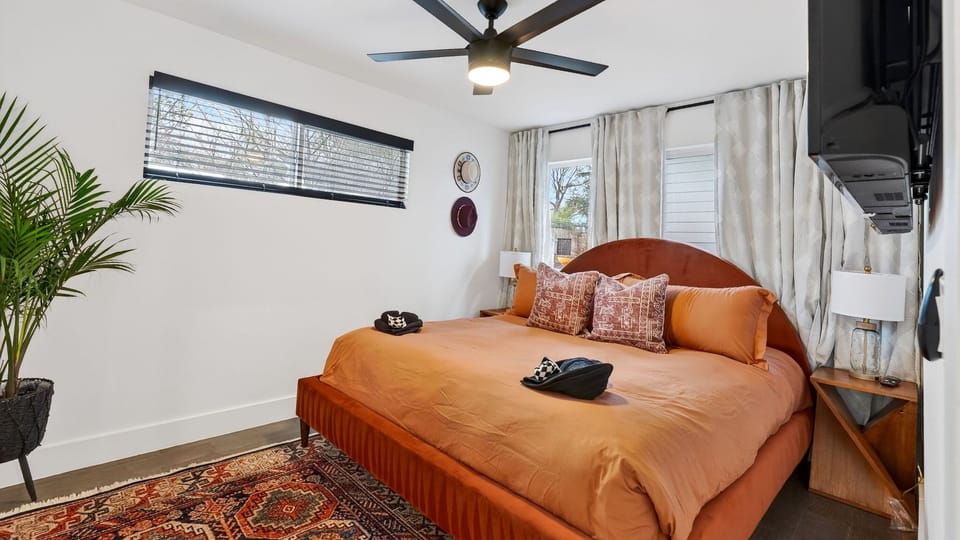 Bright bedroom with a pop of color, featuring an orange velvet bed and a geometric area rug.