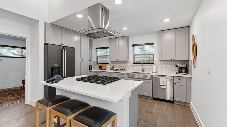 Modern kitchen with grey cabinetry, white quartz countertops, and a central island with a built-in cooktop.