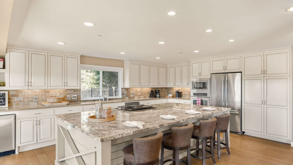 Expansive white kitchen with a massive granite island and breakfast bar seating. (Main house)