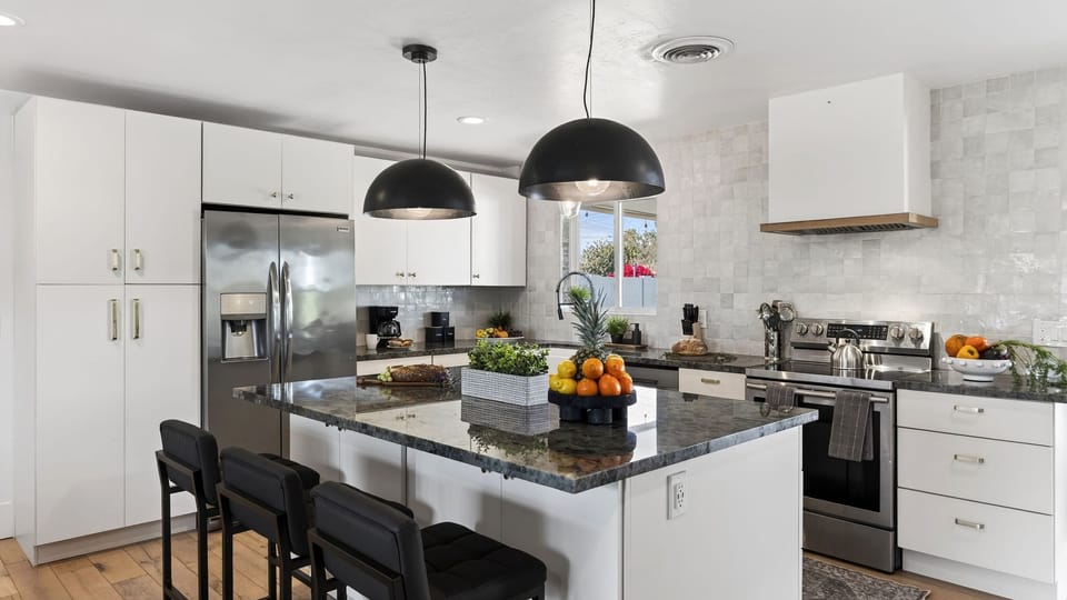 Modern kitchen with a large granite island and industrial pendant lighting.
