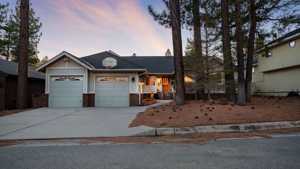 Charming Big Bear mountain retreat surrounded by towering pines with a welcoming, warmly lit entrance.