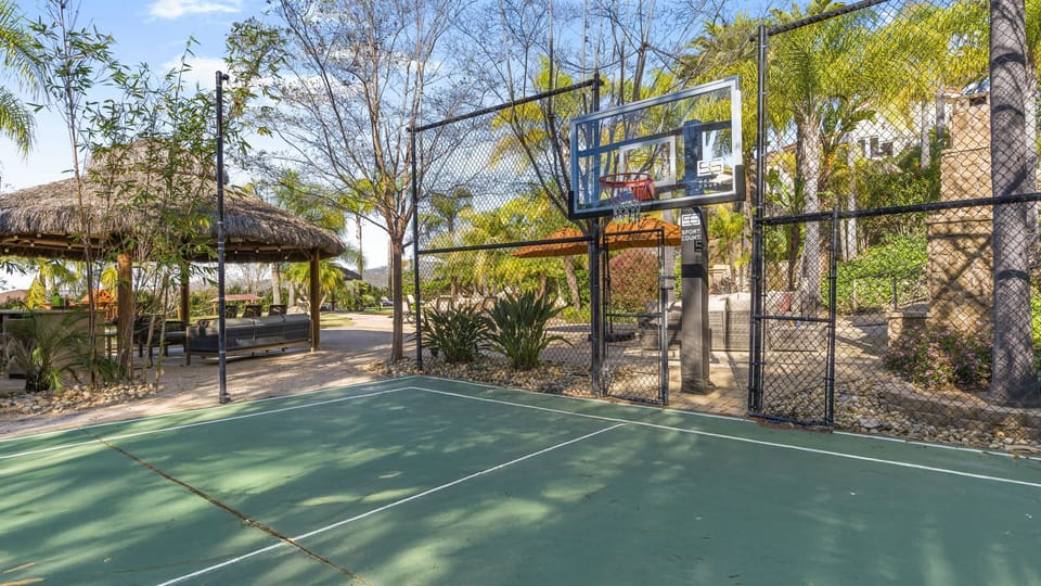 Private basketball court surrounded by palms, with a shaded tiki‑style lounge just steps away.