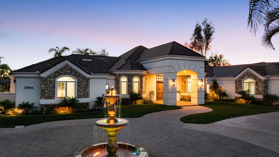 Grand Mediterranean‑style entrance with a circular drive, tiered fountain, and manicured palms.