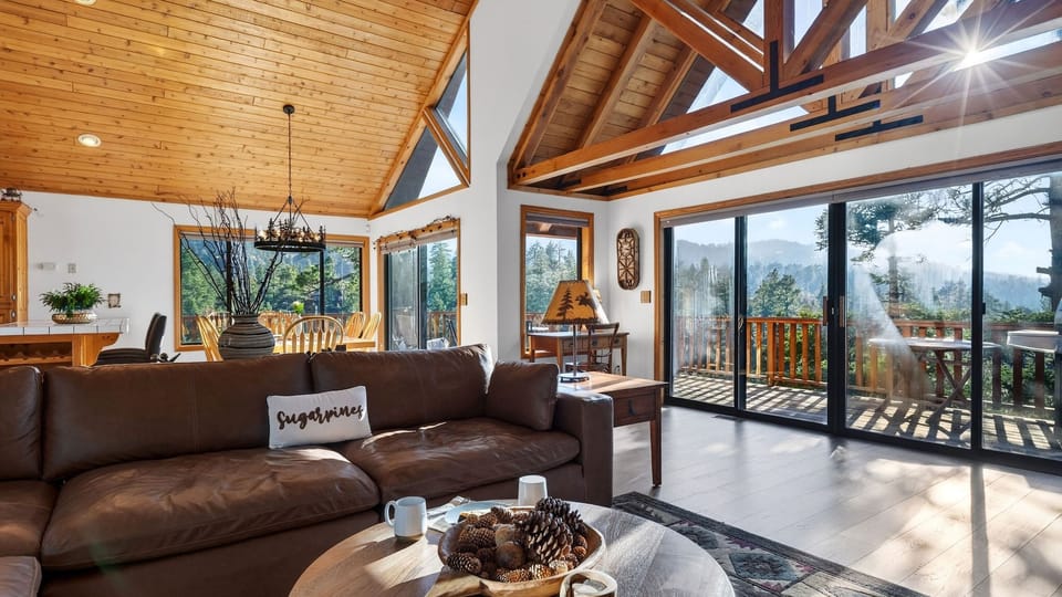 Cozy cabin living room with a leather sectional, stone fireplace, and warm wood‑beam ceilings.