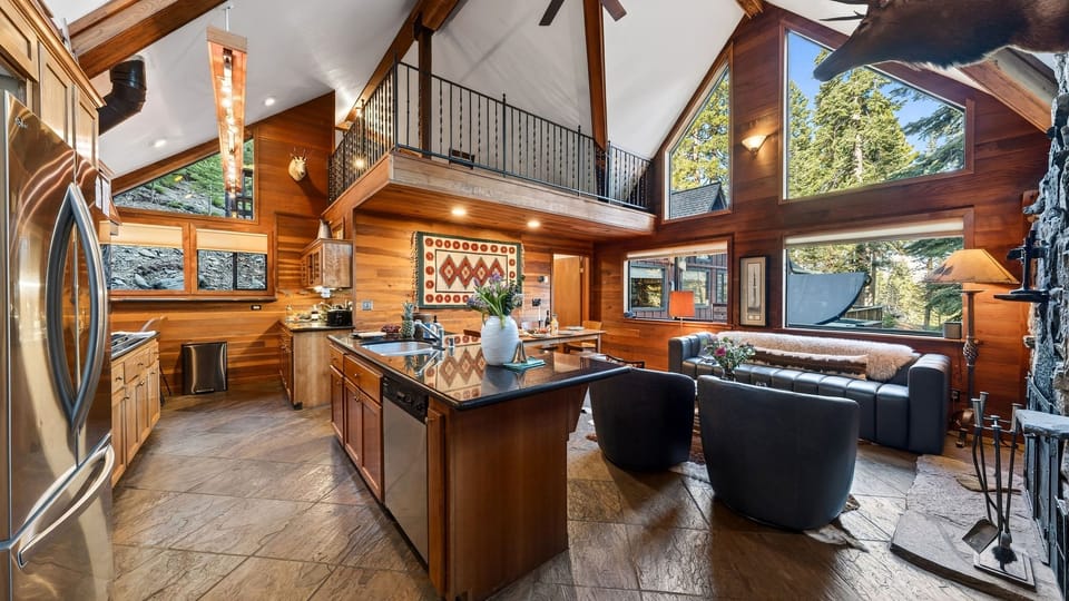 Warm, vaulted cabin interior with towering windows, rustic wood finishes, and a stone fireplace anchoring the open‑concept living space.