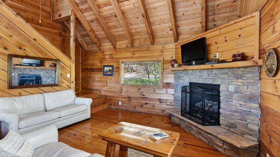 Cozy up by the stone fireplace in this warm, wood-lined living space—perfect for relaxing evenings after a day in the mountains.