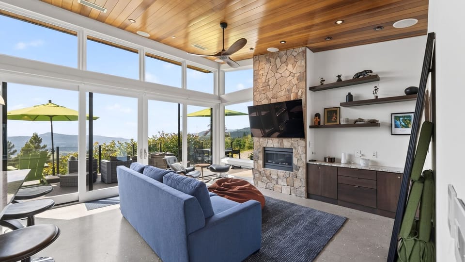 Open-concept living room with floor-to-ceiling windows and a stone fireplace.