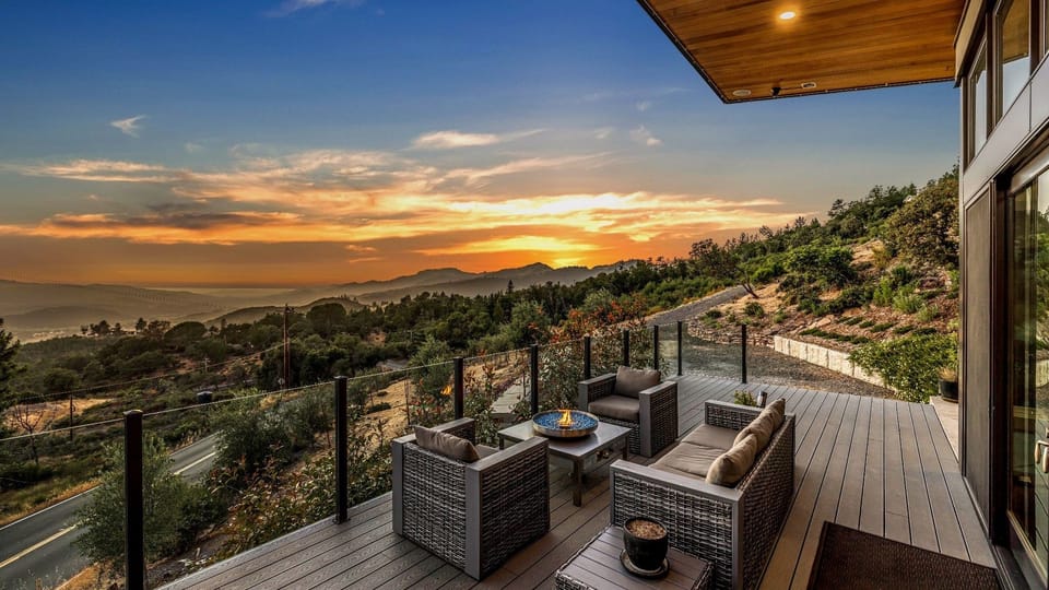 Expansive deck featuring modern lounge seating and a firepit at dusk.