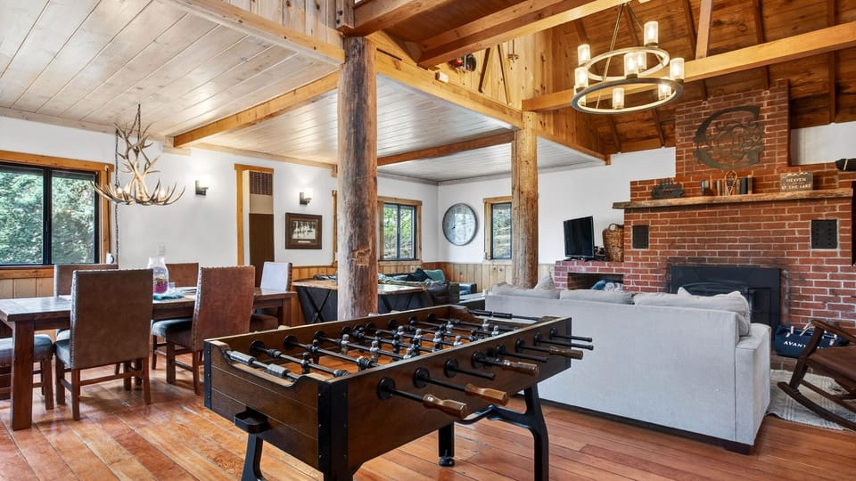 Open-concept interior with soaring ceilings, rustic wood beams, and a professional foosball table for entertainment.