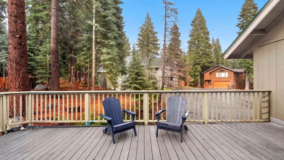 Spacious deck with Adirondack chairs overlooking peaceful forest surroundings.