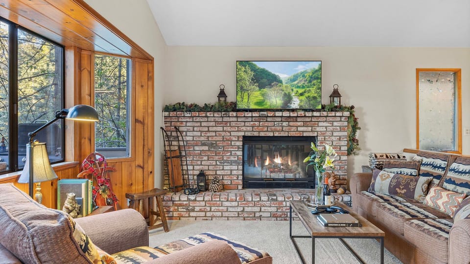 Cozy up by the fireplace in a warm mountain-style living room with forest views just outside.