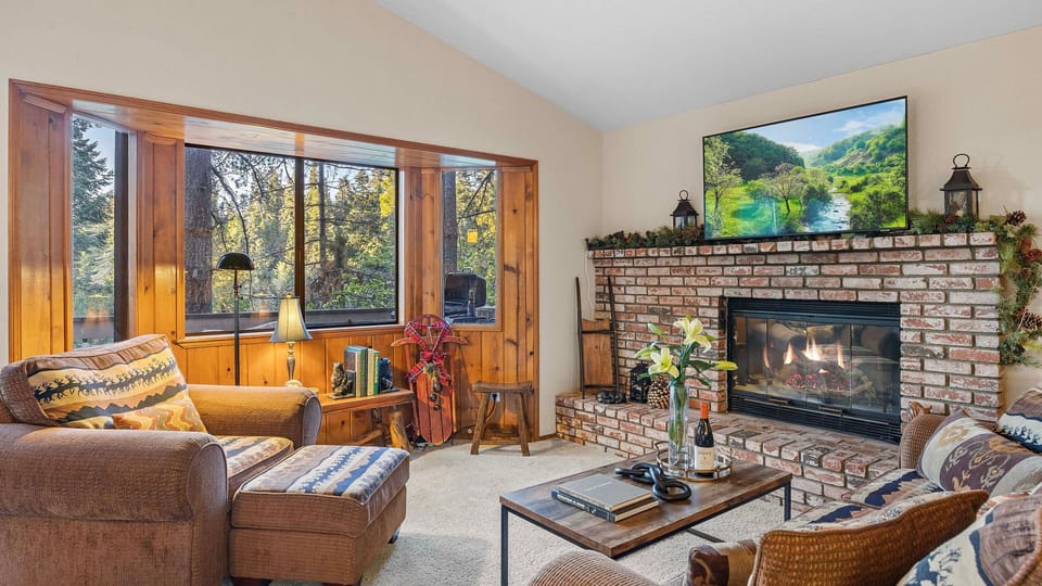 Cozy mountain living room with a brick fireplace, forest views, and warm cabin-inspired décor.