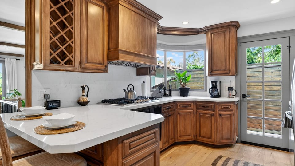 Gourmet kitchen featuring custom warm wood cabinetry, gleaming white countertops, and a glass-paneled door leading straight to the side yard.