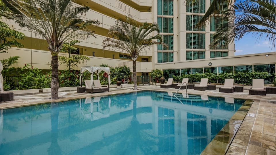 Resort-style swimming pool surrounded by lush palm trees and luxury lounge chairs.