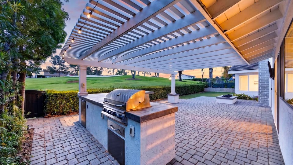 Experience ultimate outdoor living under a magnificent custom pergola, complete with a built-in BBQ island and string lighting.