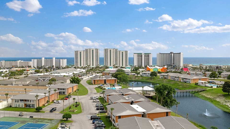 Beautiful, clear-day aerial framing the neighborhood roofs against iconic resort towers and blue ocean skies.