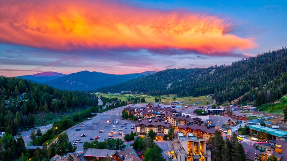 Sunset aerial view of the alpine retreat surrounded by pines and dramatic mountain scenery.