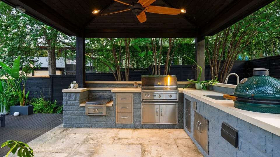 The covered outdoor kitchen comes equipped with a gas grill, ceramic smoker, sink, and generous prep space.