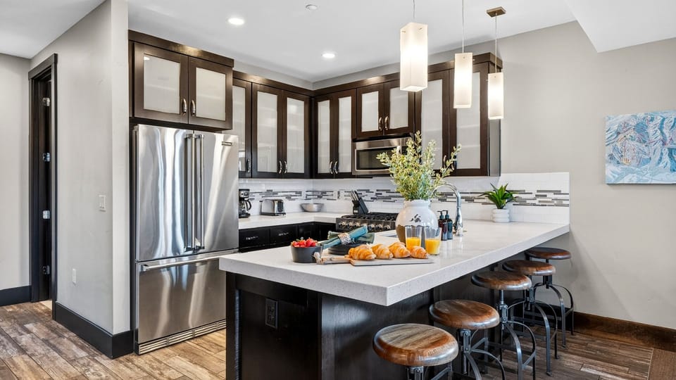 Stylish dark wood cabinetry framing a bright marble kitchen island with leather stool seating.