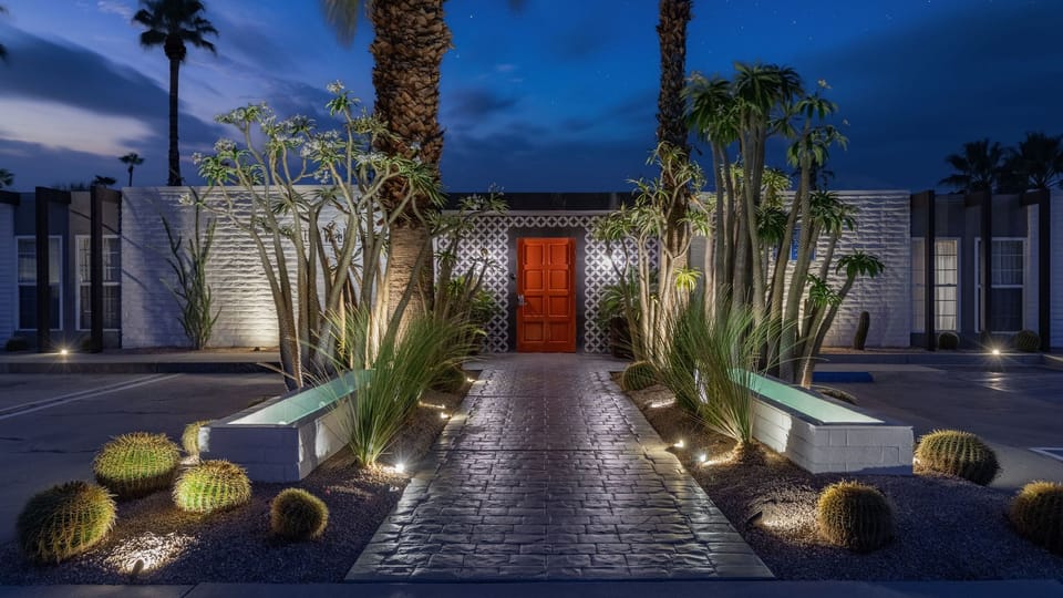 Illuminated Palm Springs entry with a bold red door, desert landscaping, and dramatic evening curb appeal.
