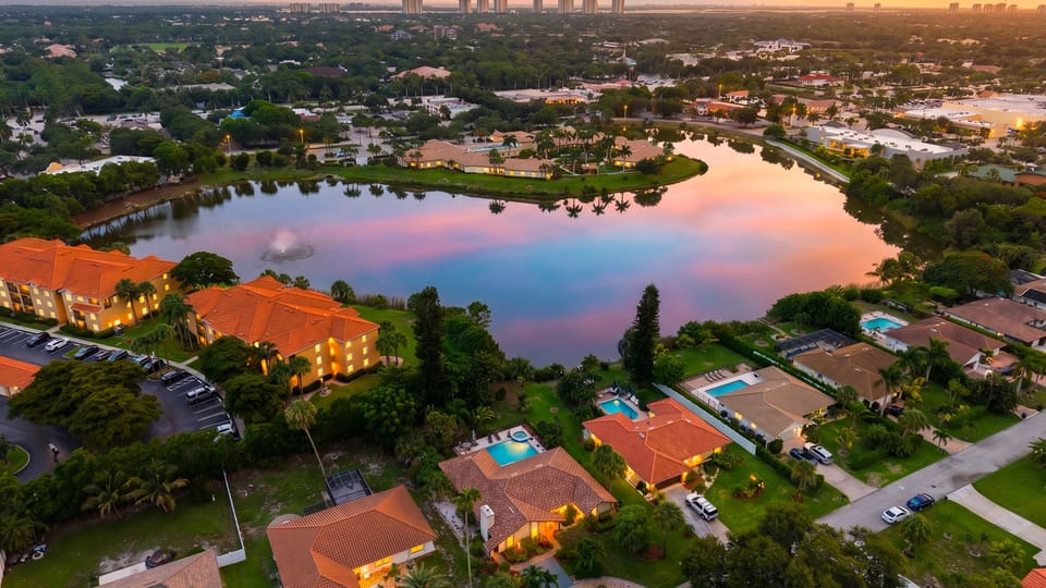 Sunset aerial showcasing the home’s tropical setting, glowing curb appeal, and lake views beyond.
