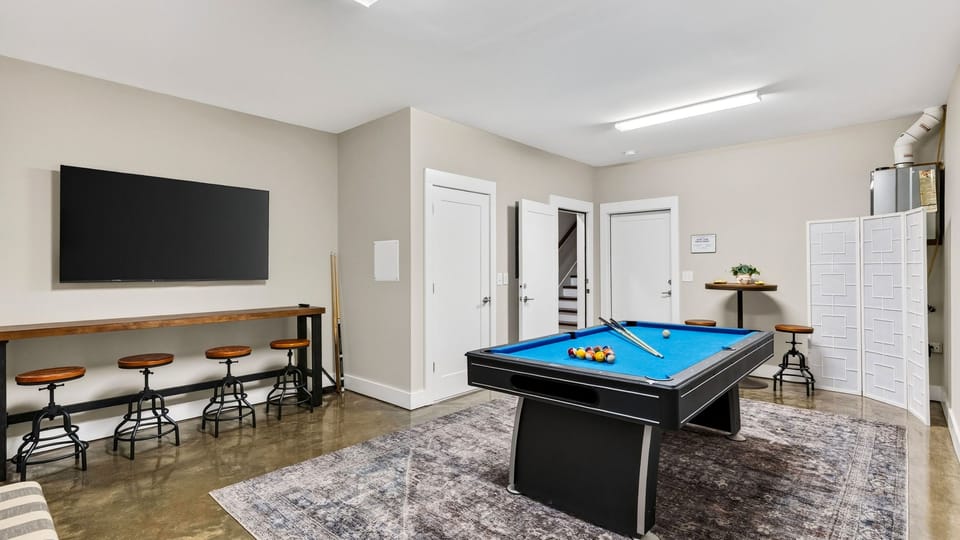 Rec room with a pool table, wall-mounted TV, pub-style seating, and plenty of space to play.