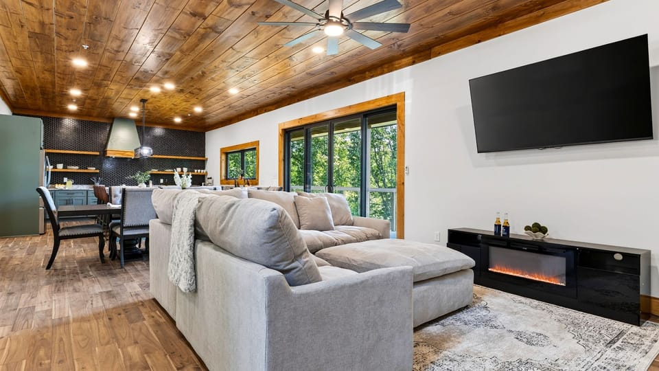 Open-concept living and dining area highlighted by warm wood ceilings and a large flat-screen TV.