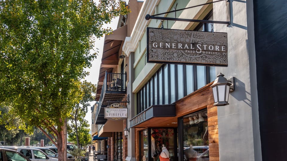 Shaded sidewalk leads past local shops and hanging signs