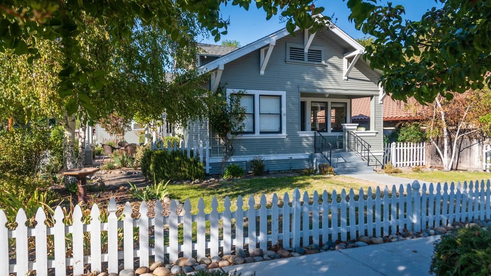 A classic cottage exterior, white picket fence, and mature trees create a warm first impression.