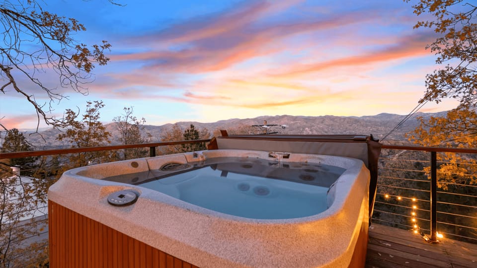 Outdoor hot tub on the deck with a vibrant sunset and mountain valley view.