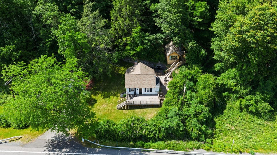 Aerial view of the cottage tucked into lush greenery, with a spacious deck and peaceful wooded setting.