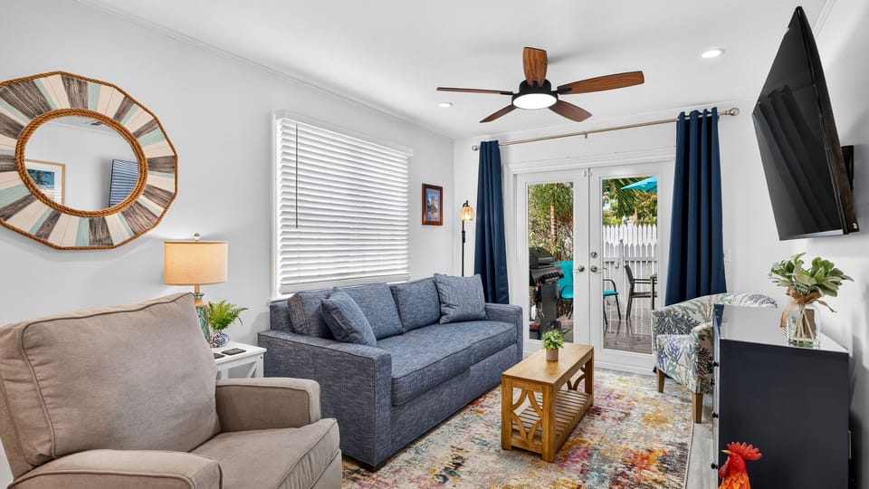 Bright living room featuring a blue sofa, coffee table, and ceiling fan.