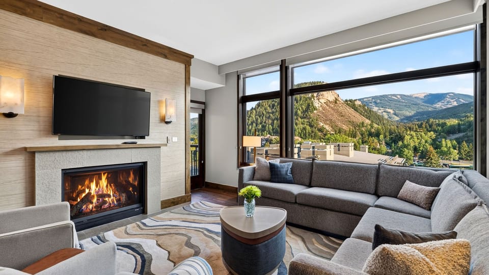 Cozy up by the fireplace in this bright living room, complete with plush seating, a large TV, and floor-to-ceiling windows.